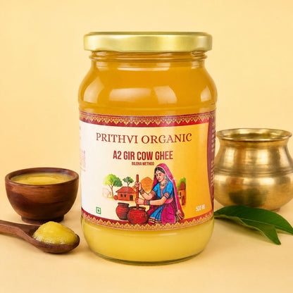 A jar of Prithvi Organic A2 Gir Cow Ghee on a warm beige background, styled with a small wooden bowl, a spoon with ghee, and a brass pot.